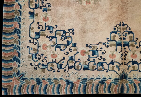 Pale pink low-pile rug corner featuring navy floral scrolls, coral blossoms, and a striped cloud border.