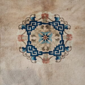 Close-up of a light beige, medium-pile rug featuring a central medallion patterned in deep blue and muted coral.