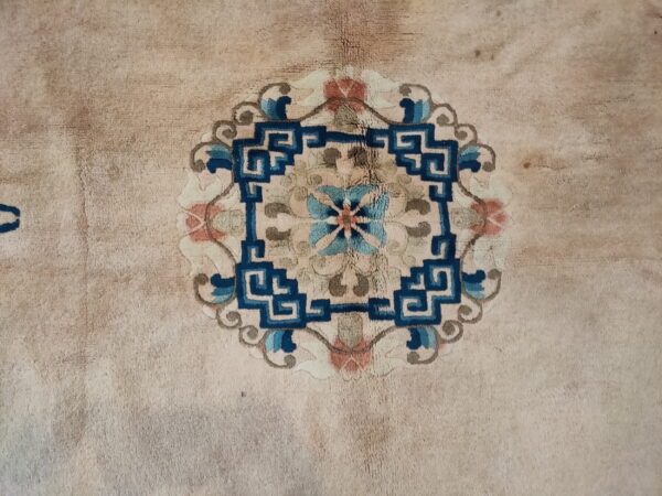 Close-up of a light beige, medium-pile rug featuring a central medallion patterned in deep blue and muted coral.