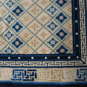 Close-up of a cream rug with blue geometric lattice, floral details, and multiple fretwork borders.