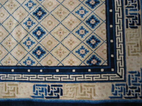 Close-up of a cream rug with blue geometric lattice, floral details, and multiple fretwork borders.