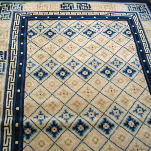 Cream rug with blue diamond lattice and interlocking key pattern borders resting on a polished wood floor.
