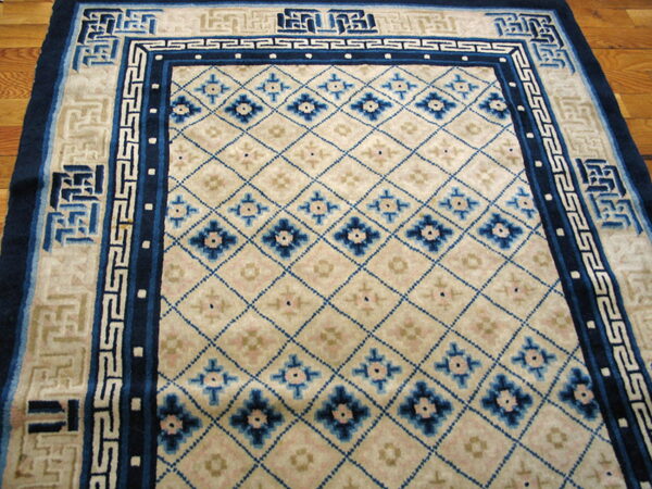 Cream rug with blue diamond lattice and interlocking key pattern borders resting on a polished wood floor.
