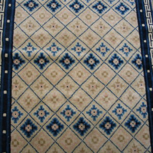 Cream rug field with a blue diamond lattice, pink accents, and geometric blue and tan borders.