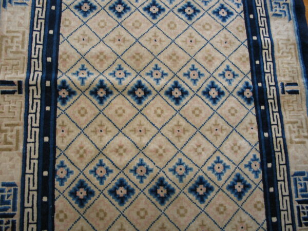 Cream rug field with a blue diamond lattice, pink accents, and geometric blue and tan borders.