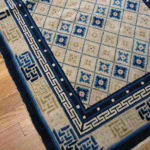 High-pile rug in ivory, dark blue, and pink with geometric field and Greek key border on wood floor.