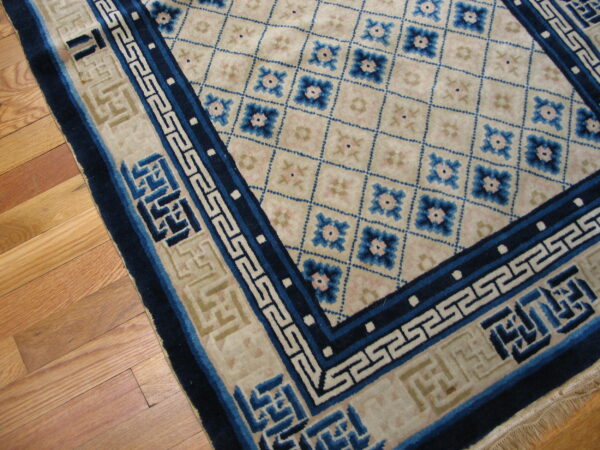 High-pile rug in ivory, dark blue, and pink with geometric field and greek key border on wood floor.