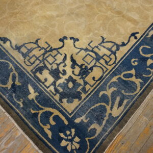 Tan rug corner with a navy blue border featuring detailed geometric and floral patterns on distressed wood floor.