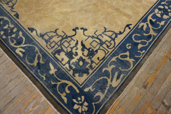 Tan rug corner with a navy blue border featuring detailed geometric and floral patterns on distressed wood floor.