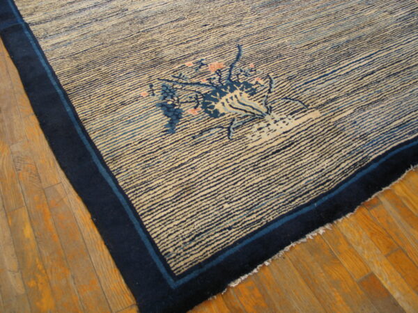 Cream rug with dense horizontal blue stripes, dark blue border, and a pink floral vase motif on hardwood.