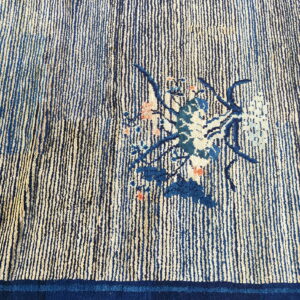 Blue and cream striped rug detail showing a small floral arrangement and a solid dark indigo border.