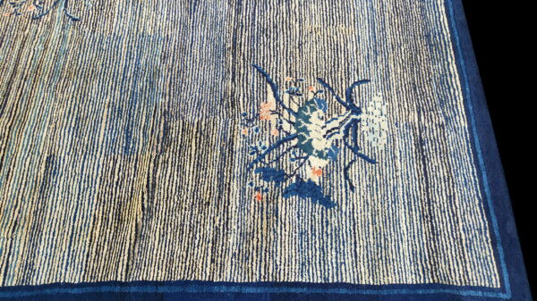 Blue and cream striped rug detail showing a small floral arrangement and a solid dark indigo border.
