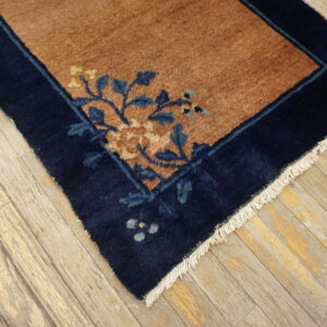 Navy border and rust field rug with blue and yellow floral pattern sits on light distressed wood planks.