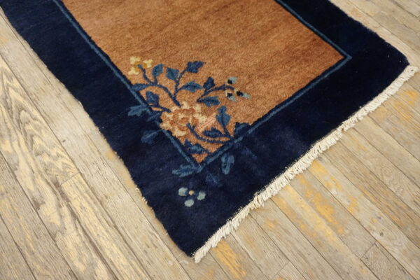 Navy border and rust field rug with blue and yellow floral pattern sits on light distressed wood planks.