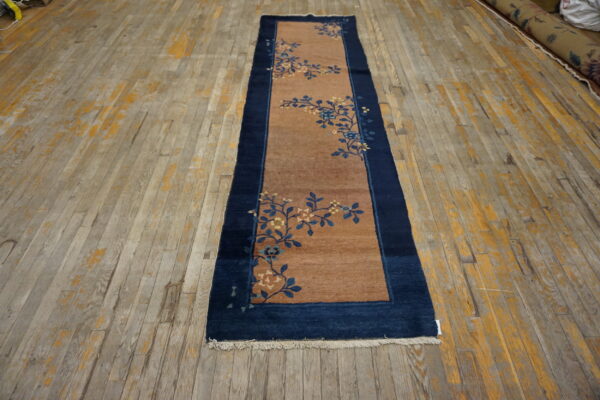Brown runner with a dark blue border and blue and gold floral sprigs on distressed wood planks.