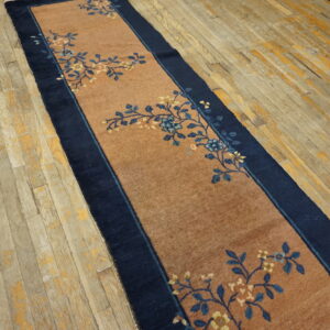 Low-pile reddish-brown runner with dark blue floral vines and border on weathered hardwood floors.