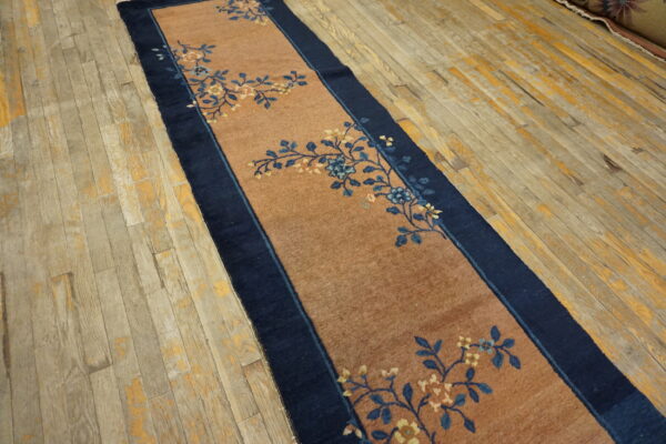 Low-pile reddish-brown runner with dark blue floral vines and border on weathered hardwood floors.