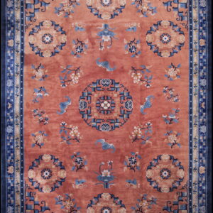 Coral-red rug with ornate blue and ivory floral medallions, stylized bats, and a deep blue geometric border.