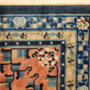 Highly detailed rug corner in coral, navy blue, yellow, and teal with traditional floral patterns on white tile.