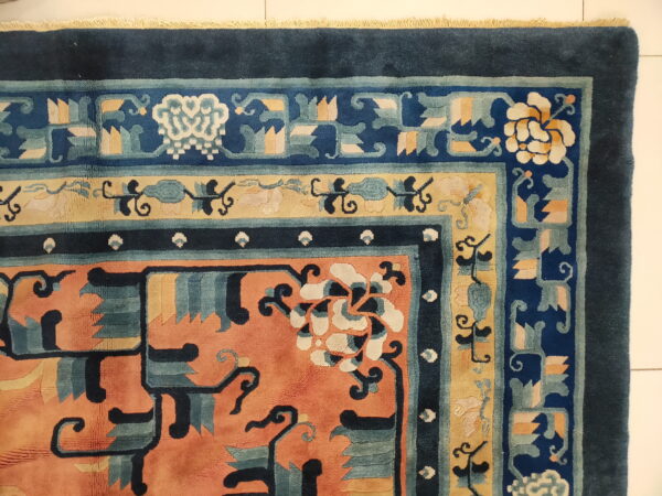 Highly detailed rug corner in coral, navy blue, yellow, and teal with traditional floral patterns on white tile.