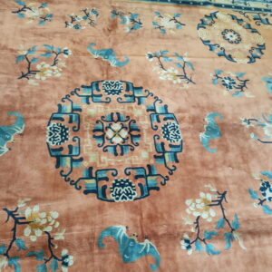 Plush salmon rug displaying a geometric medallion, stylized blue bats, and cream floral branches.