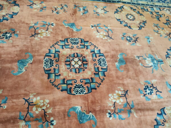 Plush salmon rug displaying a geometric medallion, stylized blue bats, and cream floral branches.