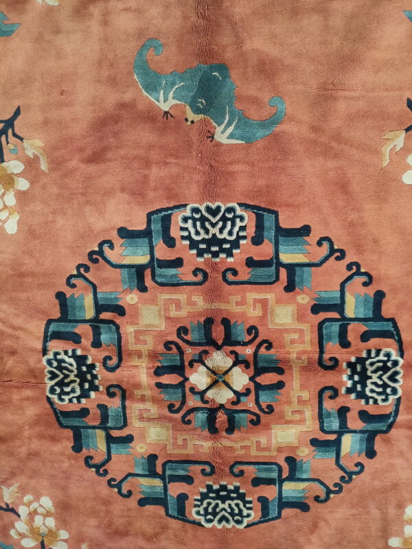 Plush salmon rug detail with a blue-green bat and multi-colored geometric central medallion design.