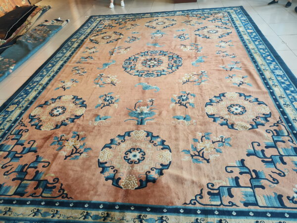 Low-pile salmon rug with blue geometric corner medallions and scattered floral motifs on white tile flooring.