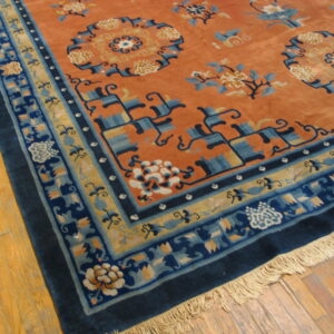 Rust-colored high-pile rug with complex navy and sky blue floral borders resting on wood plank flooring.