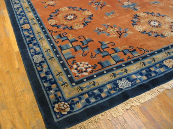 Rust-colored high-pile rug with complex navy and sky blue floral borders resting on wood plank flooring.