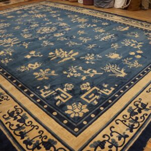 Blue and beige area rug with stylized floral patterns and multiple borders lying on wooden planks.