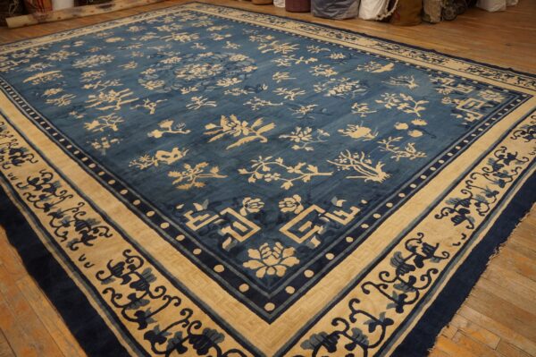 Blue and beige area rug with stylized floral patterns and multiple borders lying on wooden planks.