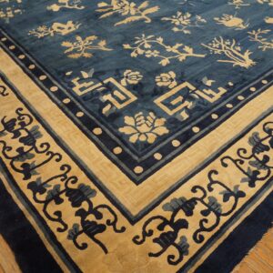 Low-pile rug with indigo and tan floral motifs and geometric borders lies on hardwood flooring.