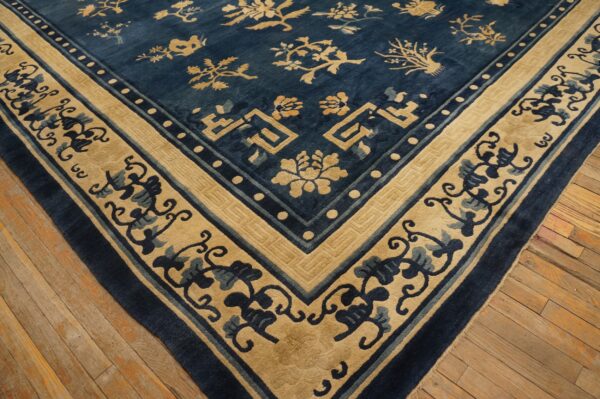 Blue and tan low-pile rug featuring stylized botanical patterns and a geometric corner border resting on wood planks.