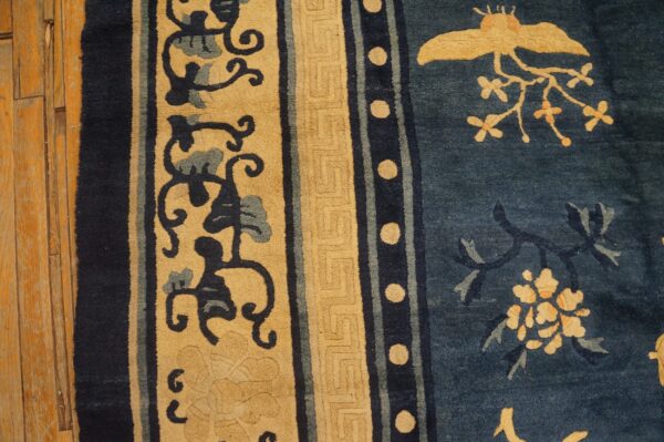 Indigo and tan rug displays detailed borders, scrolling vines, and a central bird motif over wood planks.