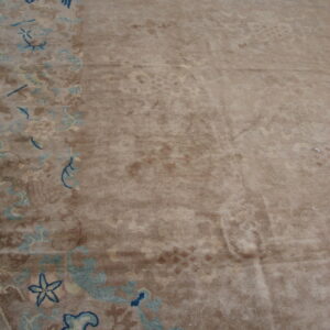 Tan pile rug close-up showing a border design with teal and dark blue traditional symbols.