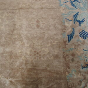 Beige rug detail showing a subtle field pattern contrasting with a dark blue and light blue border design.