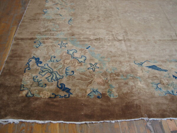 Tan and brown rug with stylized blue floral patterns and fringe on hardwood planks.