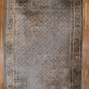 A slate gray rug with a light beige geometric pattern and floral border rests on antique wood flooring.