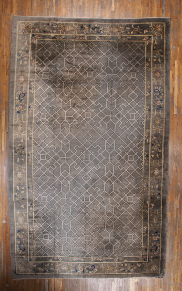 A slate gray rug with a light beige geometric pattern and floral border rests on antique wood flooring.