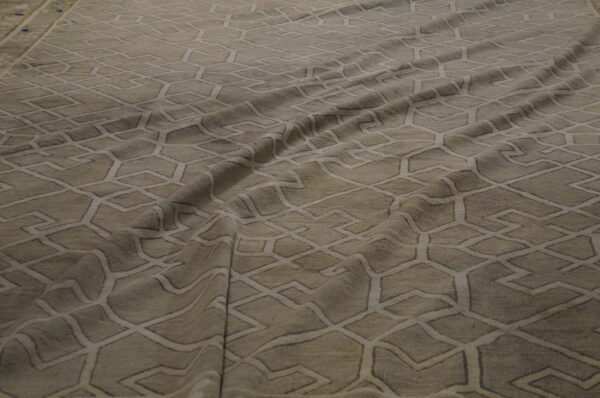 Draped beige rug features a repeating subtle geometric trellis pattern of light intersecting lines.