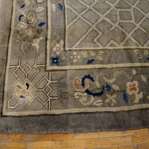 Plush gray rug with cream, blue, and coral floral motifs and geometric trellis borders on wood flooring.