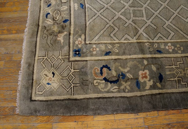 Plush gray rug with cream, blue, and coral floral motifs and geometric trellis borders on wood flooring.
