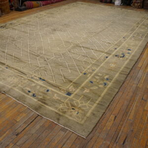 Large greige rug with a geometric trellis pattern and blue floral border, displayed on distressed wood flooring.