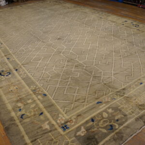 Sage rug with a geometric lattice pattern and floral border detailing in blue and cream on wood flooring.