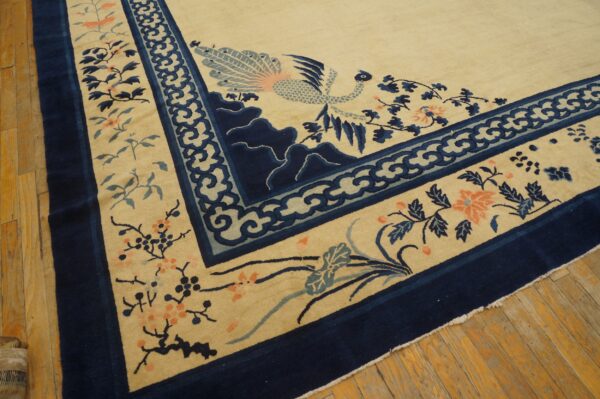 Plush cream rug with navy border and stylized bird and floral motifs rests on worn wood flooring.