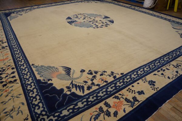 Cream high-pile rug with navy blue scrolled borders and light blue and coral bird and floral designs on wood floor.