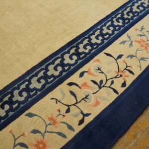 Beige rug borders show navy scrollwork and pink florals, resting on worn yellow hardwood flooring.