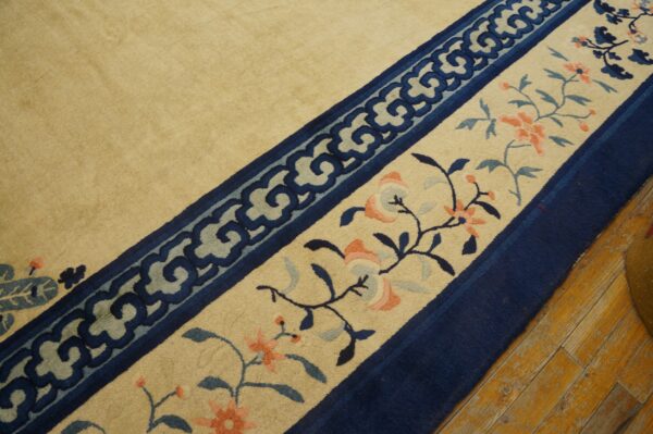Beige rug borders show navy scrollwork and pink florals, resting on worn yellow hardwood flooring.