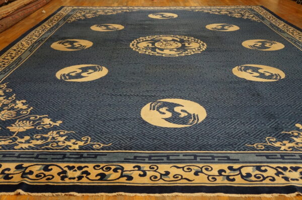 Dark blue rug with a fretwork background and cream medallions featuring stylized bird designs on wood flooring.